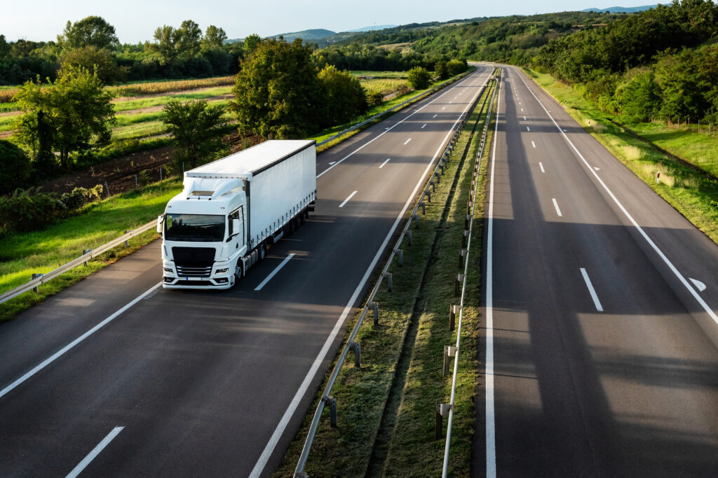 White truck driving on the highway winding through forested landscape in autumn colors at sunset